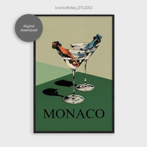 May include: A framed art print featuring two martini glasses with race cars inside. One car is orange, the other blue. The background is green and beige with the word "MONACO" in black.