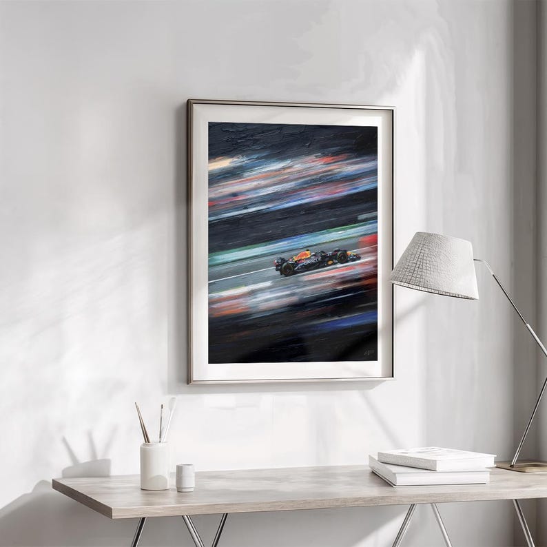May include: Framed artwork depicting a Formula 1 race car in motion. The painting features a dark background with streaks of color, suggesting speed. The car is primarily black and orange, with a blurred effect.