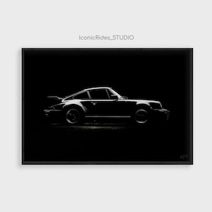 May include: A framed black and white print featuring the side profile of a sports car against a solid black background. The text IconicRides_STUDIO is printed in small grey letters at the top center of the composition.