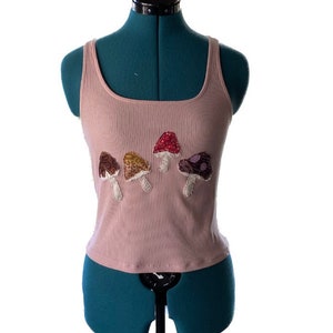 May include: A pink ribbed tank top with a row of four embroidered mushrooms in different colors.