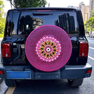 May include: A black SUV with a pink crocheted spare tire cover. The cover features a white and gold floral design.