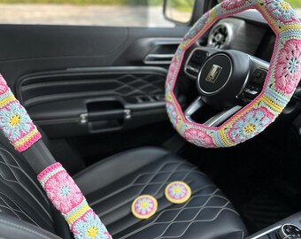May include: A set of crocheted car accessories in pink, yellow, and blue. The set includes a steering wheel cover, two seatbelt covers, and three small coasters.