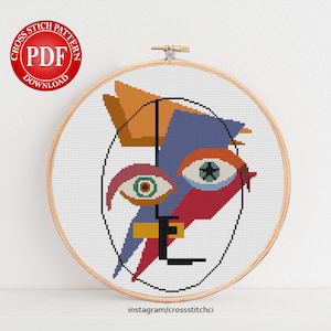 May include: Cross stitch pattern PDF download of a colorful abstract face with blue, red, orange, yellow, and green colors. The face is made up of geometric shapes and has a star in one eye.