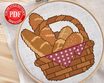 Puede incluir: Patrón de punto de cruz de una cesta llena de varios tipos de pan, incluyendo baguettes y panecillos. La cesta es marrón, forrada con un paño rojo y blanco con lunares, y colocada sobre un fondo blanco. El texto "CROSS STITCH PATTERN PDF DOWNLOAD" está en un círculo rojo.