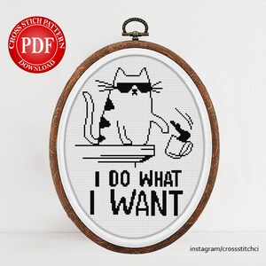 May include: A black and white cross stitch pattern of a cat wearing sunglasses and holding a coffee cup. The cat is sitting on a ledge and the text "I DO WHAT I WANT" is below the cat.