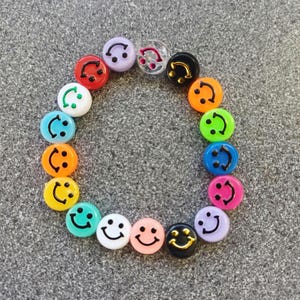 Peut inclure: Un cercle de perles de visage souriant colorées avec des contours noirs. Les perles sont disposées en cercle sur un fond gris.