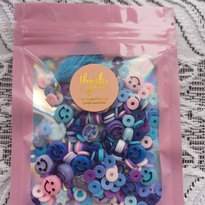 May include: A pink resealable bag filled with a variety of blue, purple, and pink smiley face and circle shaped beads. The bag has a thank you sticker with the text "thank you for supporting my small business".
