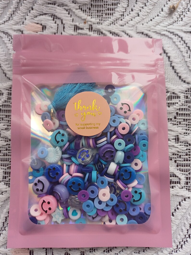May include: A pink resealable bag filled with a variety of blue, purple, and pink smiley face and circle shaped beads. The bag has a thank you sticker with the text "thank you for supporting my small business".