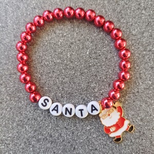 May include: Red beaded bracelet with a white 'SANTA' charm and a gold Santa Claus charm.
