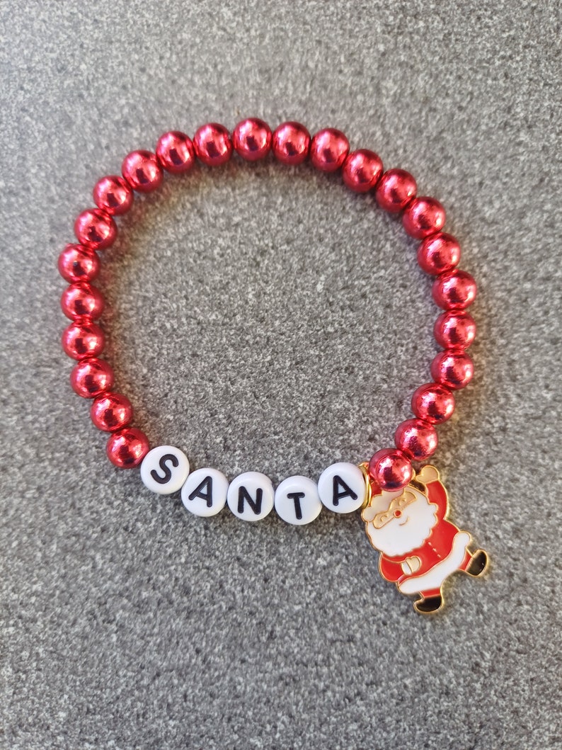 May include: Red beaded bracelet with a white 'SANTA' charm and a gold Santa Claus charm.