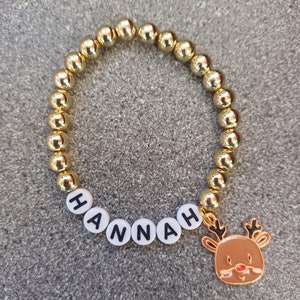 May include: Gold beaded bracelet with the name "HANNAH" spelled out in white beads and a gold reindeer charm.