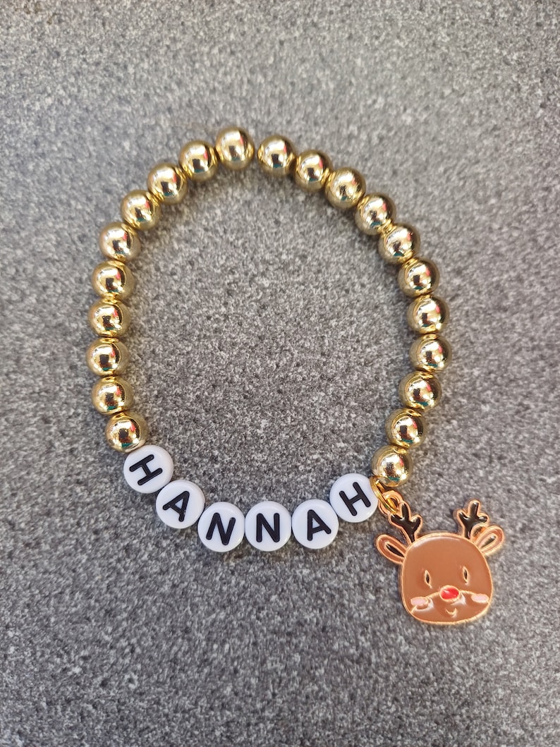 May include: Gold beaded bracelet with the name "HANNAH" spelled out in white beads and a gold reindeer charm.