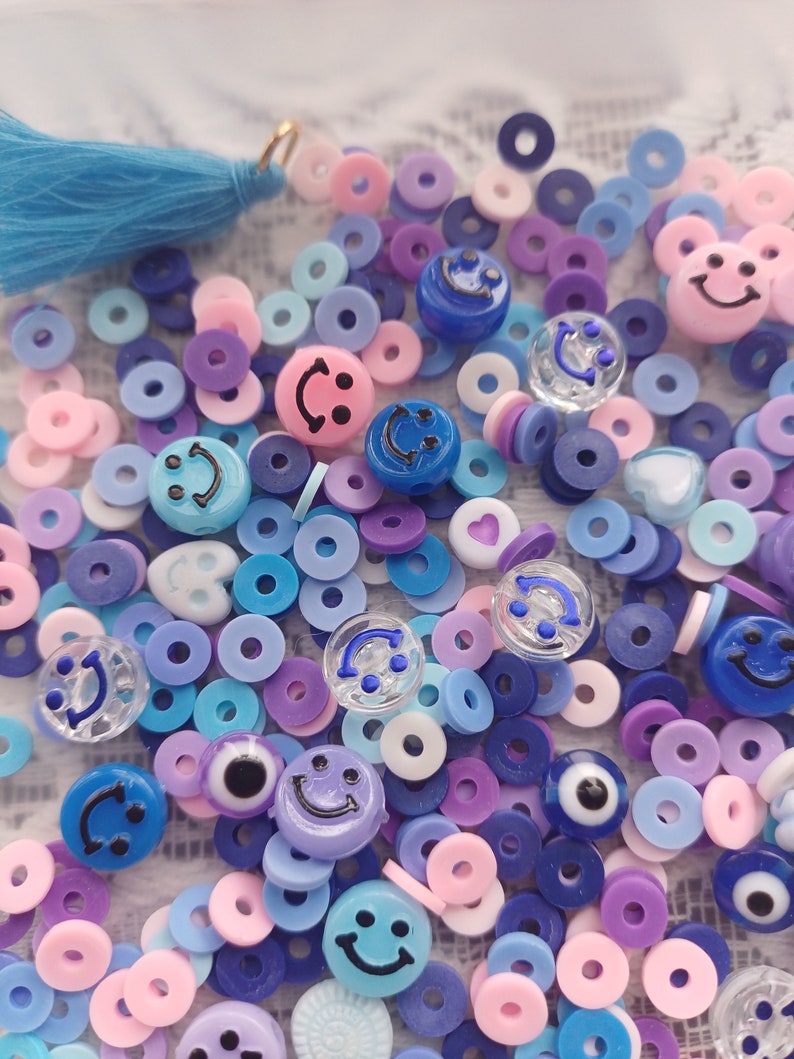May include: A variety of colorful plastic beads, including smiley faces, rings, and evil eyes. The beads are in shades of blue, pink, purple, and white.