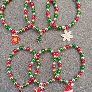 May include: Five Christmas themed bracelets with red, green, and silver beads. Each bracelet has a different charm: a mitten, a Christmas tree, a snowflake, a stocking, and a Santa hat.