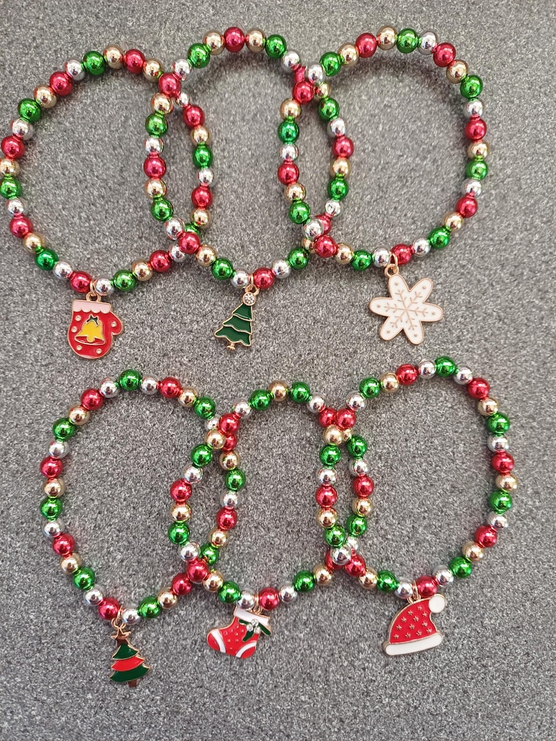 May include: Five Christmas themed bracelets with red, green, and silver beads. Each bracelet has a different charm: a mitten, a Christmas tree, a snowflake, a stocking, and a Santa hat.