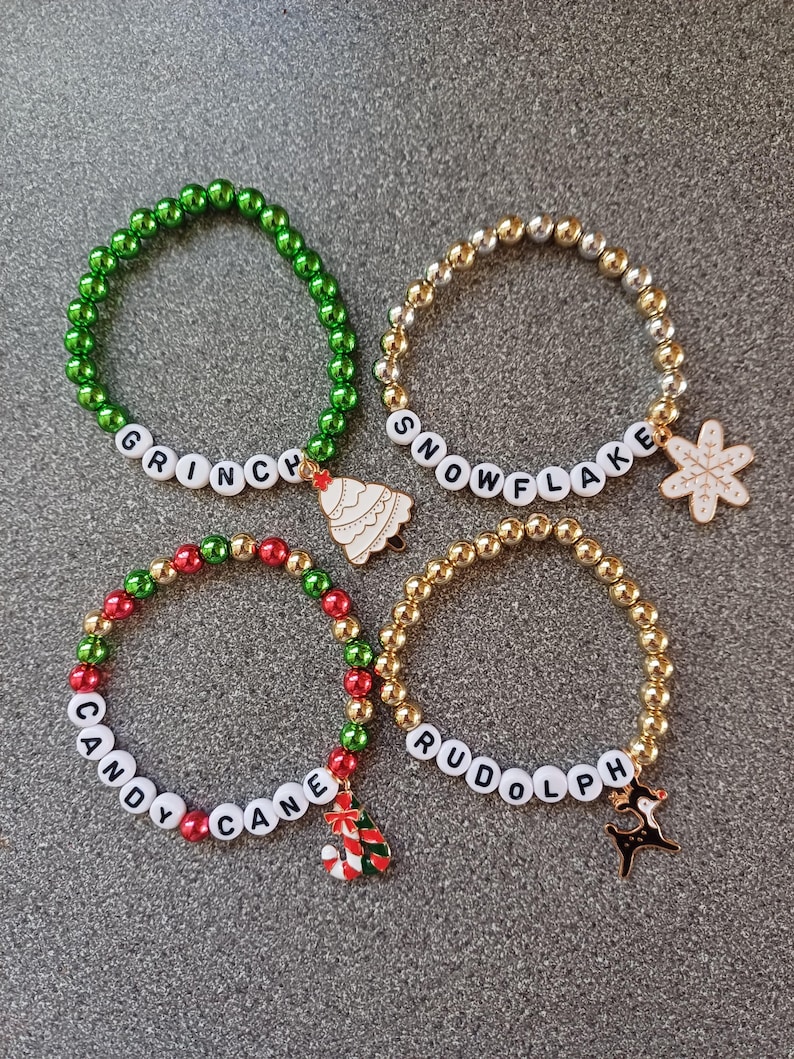 May include: Four Christmas themed beaded bracelets with charms. The bracelets are green, gold, red and gold, and gold. The charms are a Christmas tree, a snowflake, a candy cane and a reindeer.