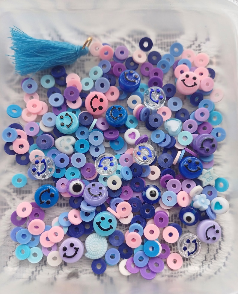 May include: A collection of colorful plastic beads in various shapes, including circles, smiley faces, and evil eyes. The beads are in shades of blue, purple, pink, and white.