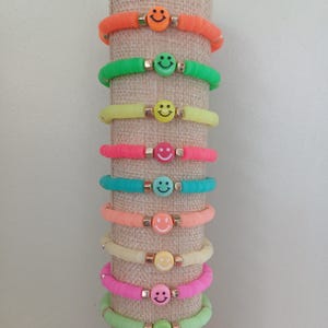 Peut inclure: Une pile de bracelets colorés avec des breloques en forme de smiley. Les bracelets sont en silicone et sont disponibles dans une variété de couleurs, notamment orange, vert, jaune, rose, bleu et vert clair.