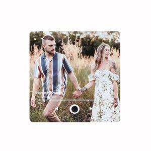 Pode incluir: Um casal de m&atilde;os dadas, caminhando pela grama alta. O homem usa uma camisa listrada e cal&ccedil;as c&aacute;qui. A mulher usa um vestido floral branco. A imagem tem uma sobreposi&ccedil;&atilde;o de reprodutor de m&uacute;sica com o texto "Because You Live" e "Jesse McCartney".