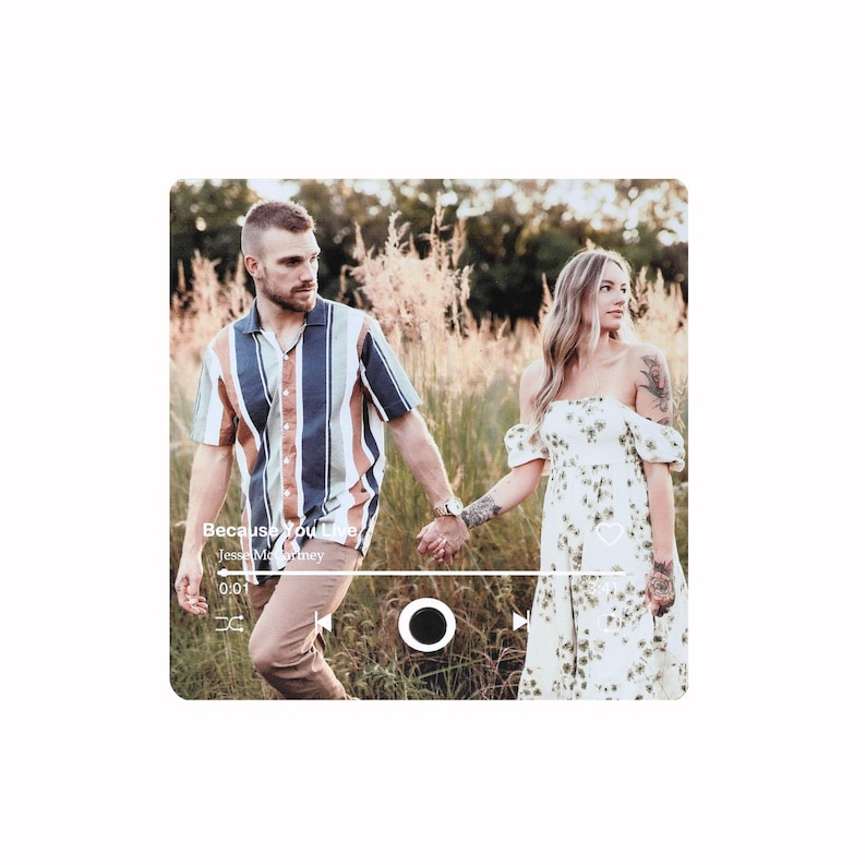 Pode incluir: Um casal de m&atilde;os dadas, caminhando pela grama alta. O homem usa uma camisa listrada e cal&ccedil;as c&aacute;qui. A mulher usa um vestido floral branco. A imagem tem uma sobreposi&ccedil;&atilde;o de reprodutor de m&uacute;sica com o texto "Because You Live" e "Jesse McCartney".