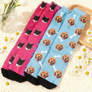 Könnte beinhalten: Drei Paar Socken mit Tiermustern. Zwei Paare sind rosa mit schwarzen Katzenköpfen, und ein Paar ist hellblau mit Golden Retriever-Gesichtern, Pfotenabdrücken und Knochen. Alle Socken haben schwarze Fersen und Zehen.