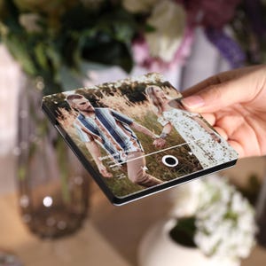 Pode incluir: Uma capa de telefone personalizada com uma foto de um casal de m&atilde;os dadas em um campo. A capa tem uma borda preta e um design de interface de reprodutor de m&uacute;sica. O texto "Because You" &eacute; vis&iacute;vel.