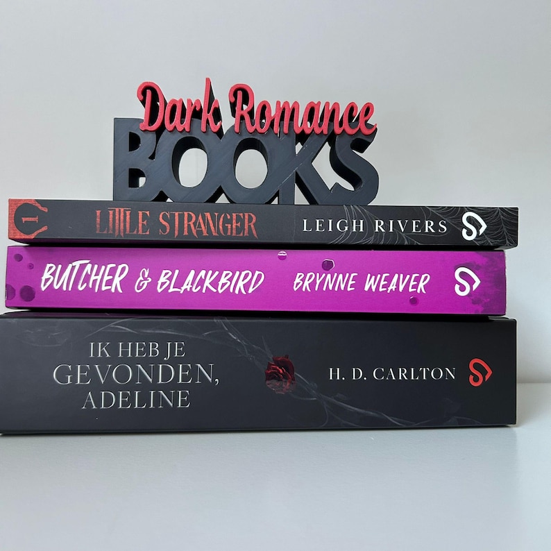 May include: A stack of three books with the words "Dark Romance BOOKS" in a decorative sign on top. The book titles are "Little Stranger", "Butcher & Blackbird", and "Ik Heb Je Gevonden, Adeline". The books have black and purple covers.