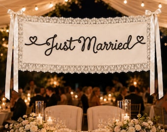 May include: A rectangular cream-colored fabric banner featuring the black script text Just Married with a heart at each end. The banner is bordered by intricate white lace trim and features long satin ribbons tied at the top corners.