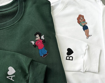 Könnte beinhalten: Zwei grün-weiße Sweatshirts mit gestickten Comicfiguren und Herzen. Das grüne Sweatshirt hat einen Comic-Hund mit einem roten Shirt und dem Text "A" mit einem Herz. Das weiße Sweatshirt hat eine Comic-Frau mit einem roten Shirt und dem Text "B" mit einem Herz.