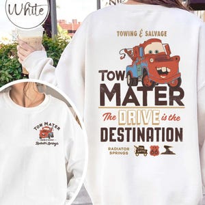 May include: White sweatshirt featuring a cartoon image of Tow Mater, a red and blue tow truck, with the text "TOW MATER" and "The DRIVE is the DESTINATION." The design includes "Towing & Salvage" and "Radiator Springs."
