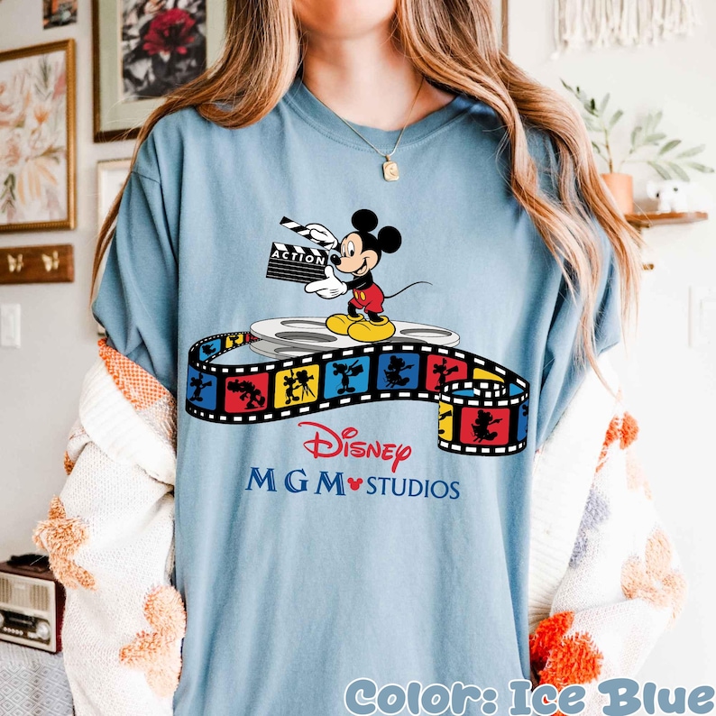 Pu&ograve; includere: T-shirt blu ghiaccio con Topolino che tiene una clapperboard, in piedi su una bobina di film. Una striscia di pellicola colorata con personaggi Disney e la scritta "Disney MGM Studios" &egrave; sotto.