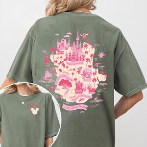 May include: Olive green t-shirt featuring a pink map design of Walt Disney World, including Magic Kingdom, Animal Kingdom, and Hollywood Studios. The front of the shirt has a small pink Mickey Mouse head graphic.