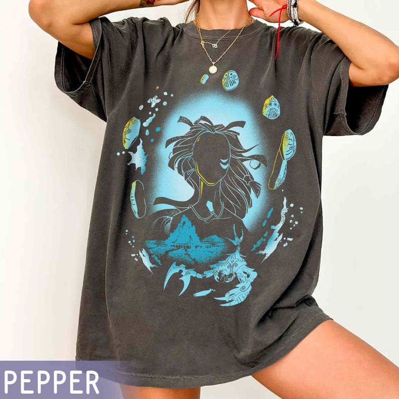 May include: A dark gray oversized t-shirt with a graphic print of a woman's silhouette with a blue and green background. The graphic includes a stylized image of a sea creature and other abstract shapes.