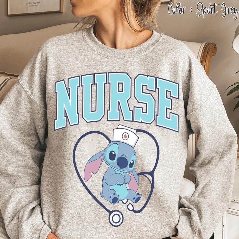 May include: Sport grey sweatshirt with the word "NURSE" in light blue block letters. Below the word is a cartoon character wearing a nurse's hat, inside a stethoscope-shaped heart.