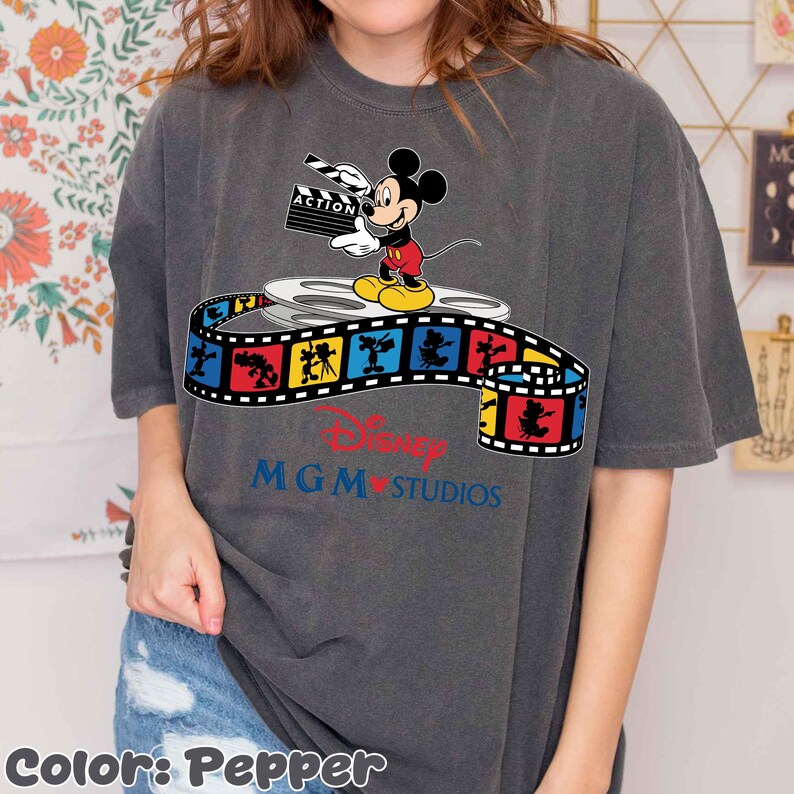 Pu&ograve; includere: T-shirt color pepe con Topolino che tiene una clapperboard, in piedi su una bobina di film. Una striscia di film colorata con personaggi Disney avvolge la bobina. Il logo Disney MGM Studios &egrave; sotto.