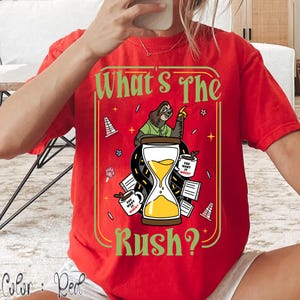 Puede incluir: Camiseta roja con un gr&aacute;fico que presenta un perezoso, un reloj de arena y el texto "What's The Rush?". El dise&ntilde;o incluye tazas de caf&eacute; y elementos de carretera, con la frase "You want it when?" en las tazas.