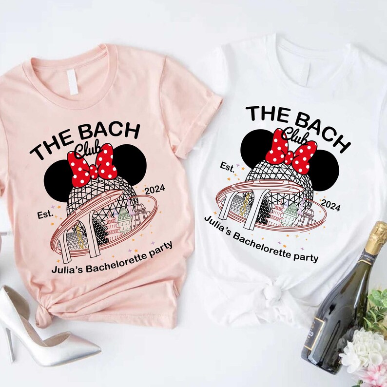 May include: Two t-shirts, one pale pink and one white, with a bachelorette party design. The design includes the text "THE BACH Club" with a Minnie Mouse-style bow and ears, the year "2024", and the text "Julia's Bachelorette party".