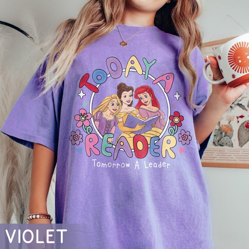 May include: Violet t-shirt with a graphic featuring three cartoon princesses reading a book, surrounded by flowers and the text "TODAY A READER Tomorrow A Leader."
