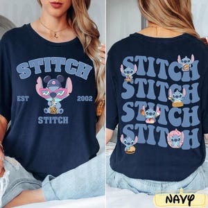 May include: Navy blue t-shirt featuring a cartoon Stitch character wearing sunglasses and holding a drink, with the word "STITCH" above and below the character. The back of the shirt has multiple Stitch graphics and the word "STITCH".