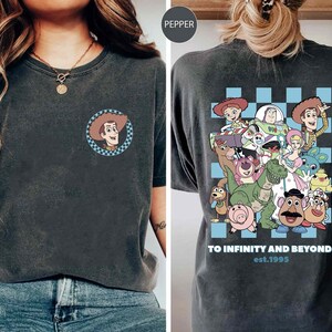 May include: A black t-shirt with a blue and white checkered pattern and a graphic of characters from the Toy Story movie franchise. The text "To Infinity and Beyond! est. 1995" is printed on the shirt.