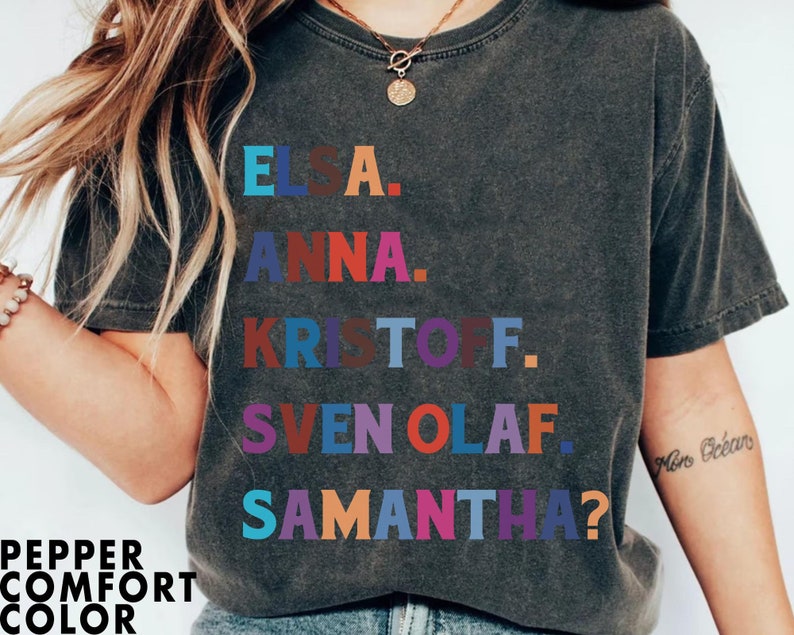 以下が含まれることがあります： 「エルサ」、「アナ」、「クリストフ」、「スヴェンオラフ」、そして「サマンサ？」という名前がカラフルなブロックレターでプリントされた、濃いグレーのTシャツ。「Pepper Comfort Color」の文字が下部にプリントされています。