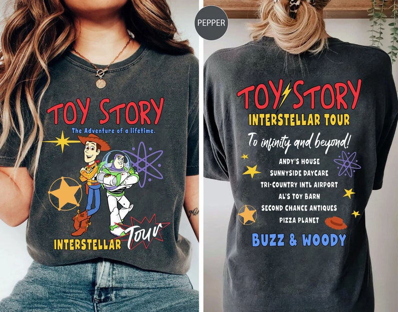 May include: Dark gray t-shirt featuring the words "TOY STORY" in red, with Woody and Buzz Lightyear graphics. The front of the shirt also says "INTERSTELLAR TOUR". The back of the shirt says "INTERSTELLAR TOUR" and "To infinity and beyond!" with a list of locations.
