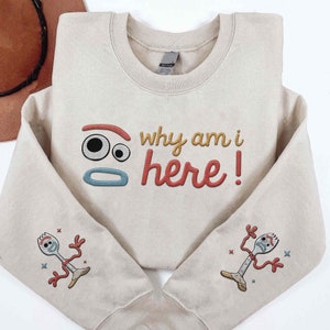 May include: A beige sweatshirt with the phrase "Why am I here!" in colourful embroidered letters. The sweatshirt also features a cartoon face and a cartoon character with a fork on each sleeve.