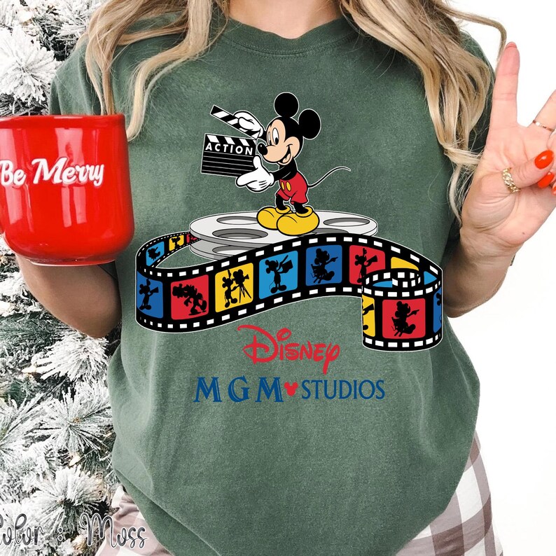 Pu&ograve; includere: T-shirt verde con Topolino che tiene una clapperboard, in piedi su una bobina di film. Una striscia di film colorata con il logo Disney MGM Studios &egrave; sotto. La tazza rossa dice "Be Merry".