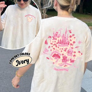 May include: Ivory-colored t-shirt with a pink graphic of the Walt Disney World map on the back and a Mickey Mouse logo on the front. The shirt is labeled "Comfort Colors" and "Ivory".