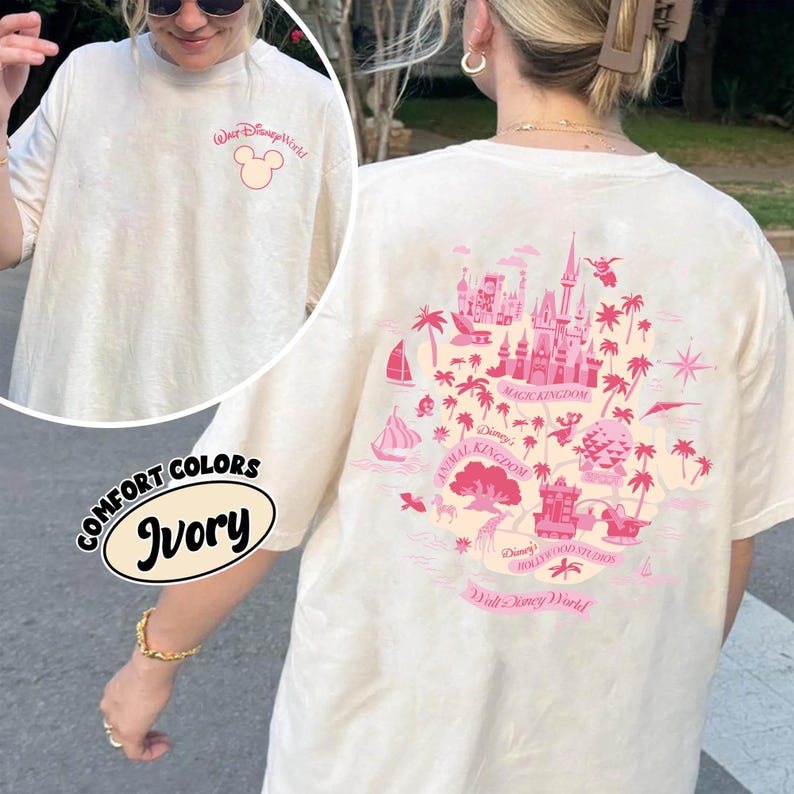 May include: Ivory-colored t-shirt with a pink graphic of the Walt Disney World map on the back and a Mickey Mouse logo on the front. The shirt is labeled "Comfort Colors" and "Ivory".
