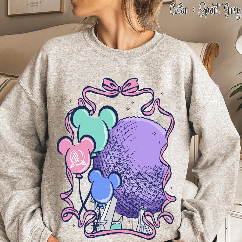 May include: Sport grey sweatshirt featuring a colorful graphic. The design includes a purple sphere, reminiscent of a geodesic dome, with three mouse-shaped balloons in blue, pink, and teal. Pink ribbons and a bow frame the central image.