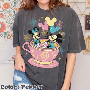 May include: Dark grey t-shirt with a graphic of Mickey and Minnie Mouse in a pink teacup, balloons, and fireworks. The text "Color: Pepper" is at the bottom of the shirt.
