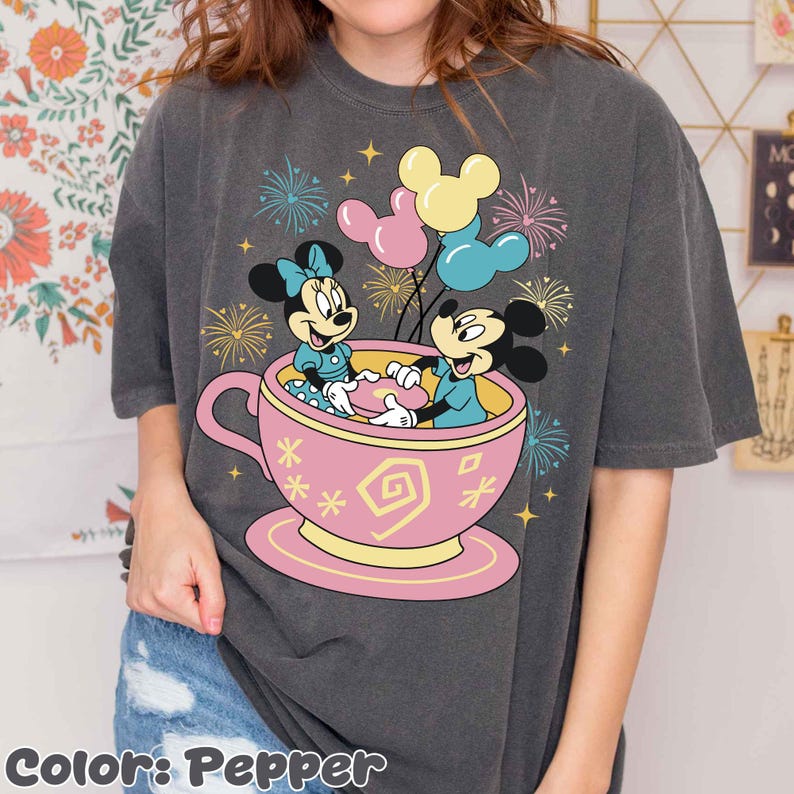 May include: Dark grey t-shirt with a graphic of Mickey and Minnie Mouse in a pink teacup, balloons, and fireworks. The text "Color: Pepper" is at the bottom of the shirt.