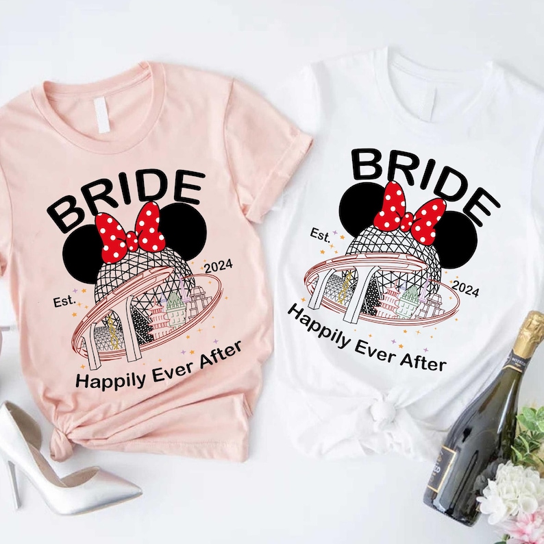 May include: Two t-shirts, one pink and one white, with a bride-themed graphic. The design includes the word "BRIDE" in black, a Minnie Mouse bow, and a theme park illustration. The text "Happily Ever After" and "2024" are also included in the design.